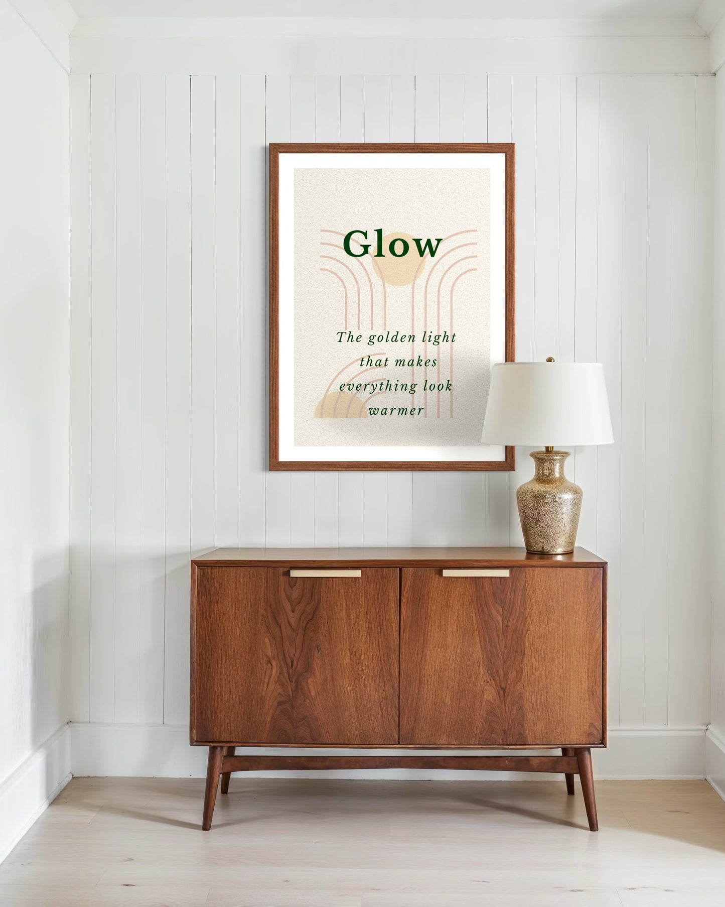 Wooden sideboard with a lamp and framed artwork on a white wall.